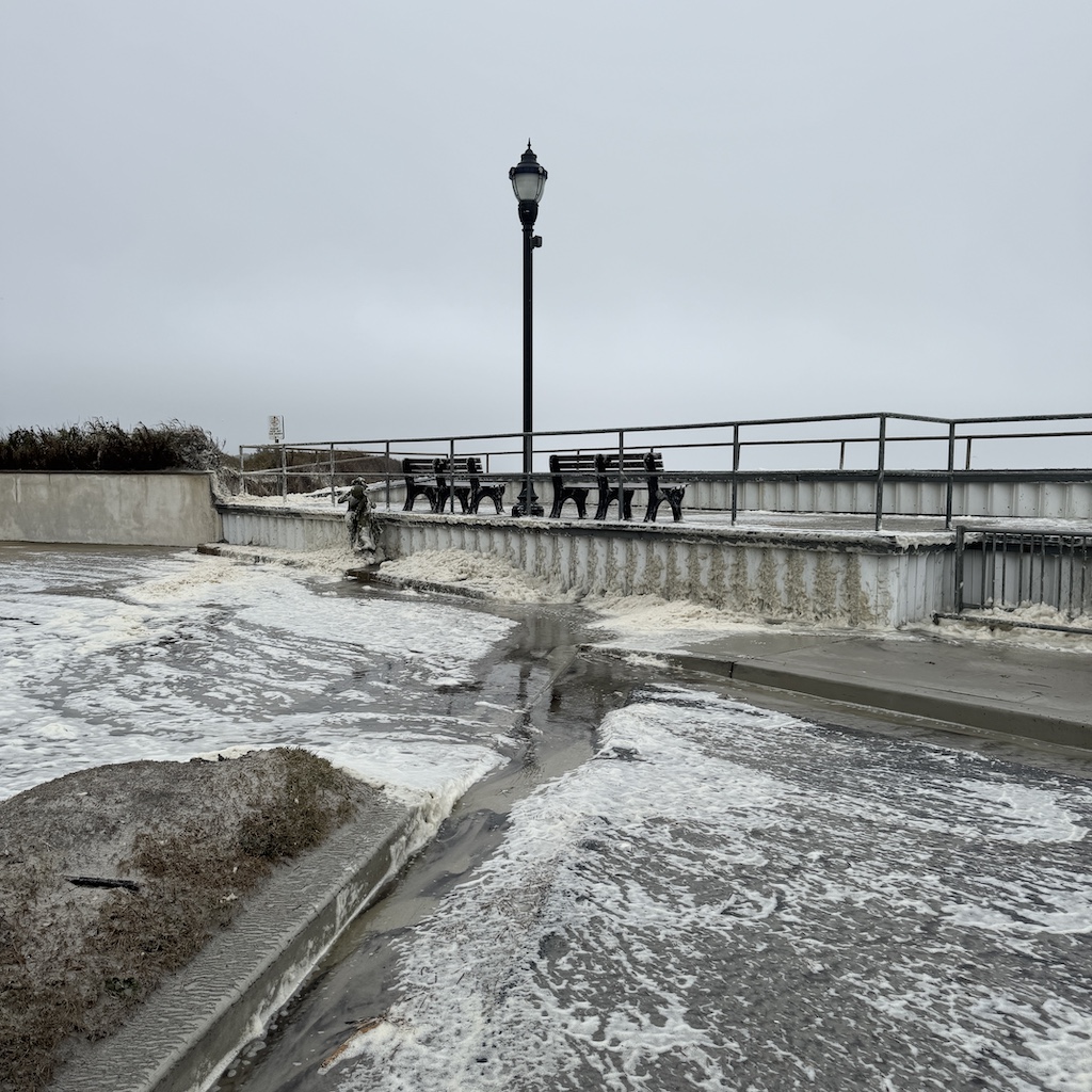 Sea foam blows into drifts on the sidewalk, Monday, October 13, 2025.