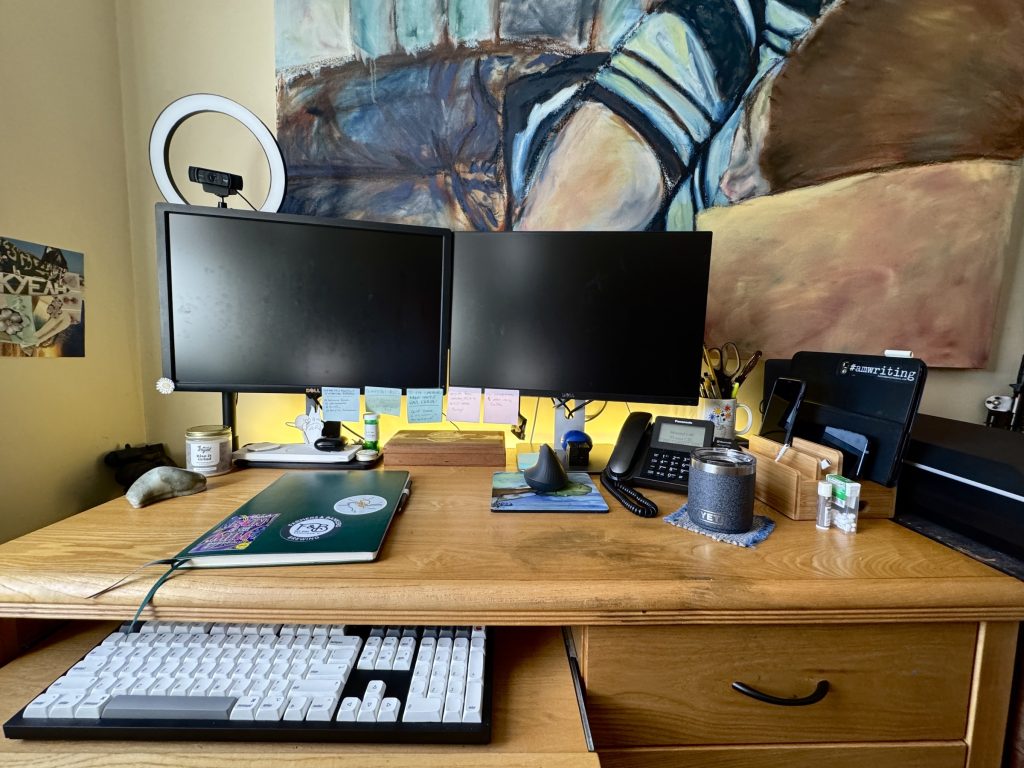 Photo of the author's desk. Surface is clean and tidy, with a large notebook in the middle.